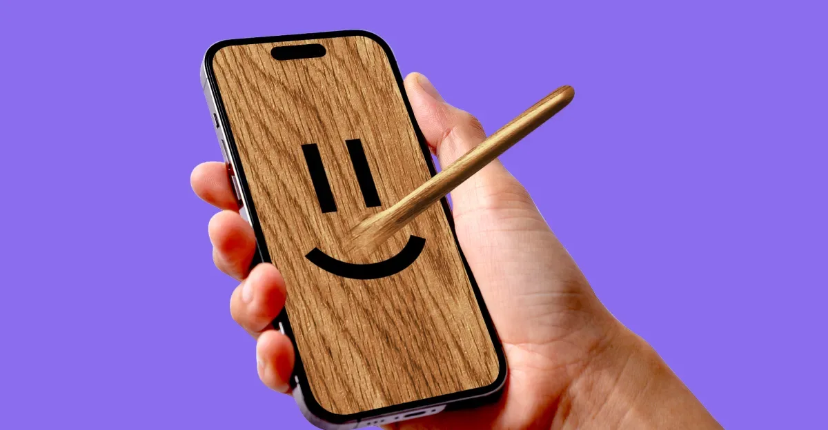 Person’s hand holding a phone with a wooden face and Pinocchio nose.