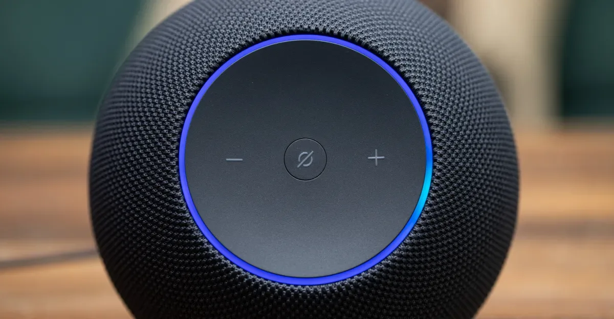 The Amazon Echo Studio with its front blue LED ring illuminated while sitting on a wooden coffee table.